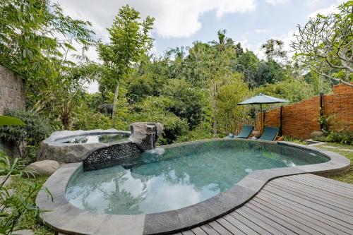 a pool in the middle of a garden with two chairs at Agastya Ubud Villa in Ubud