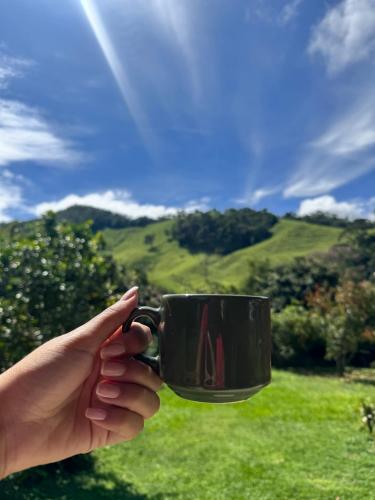 a person holding a black coffee mug with a green field at Pousada Dona Chica in Visconde De Maua