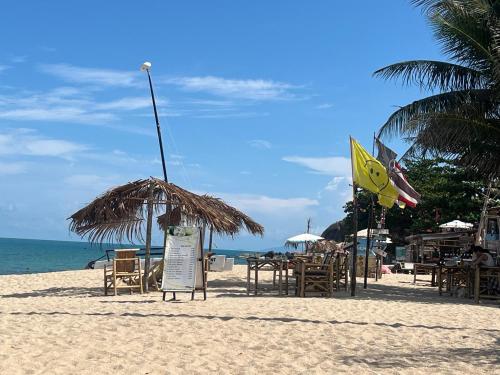 een strand met stoelen en tafels en een rieten parasol bij Paradise Bungalows Lamai Beach in Koh Samui 