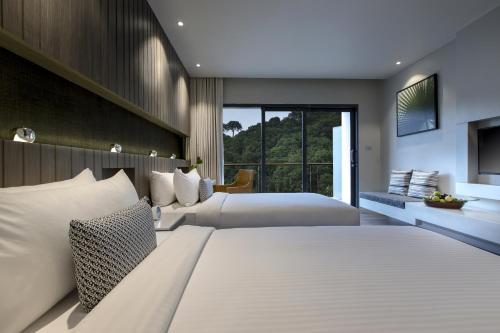 a bedroom with two beds and a large window at Hotel IKON Phuket - SHA Extra Plus in Karon Beach