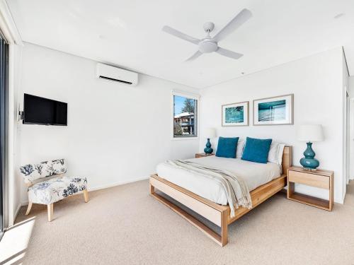 a white bedroom with a bed and a chair at White Sails 4 - Amazing views over Convent in Yamba