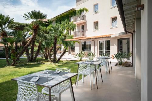 un patio con mesas, sillas y palmeras en Marina Garden Hotel, en Marciana Marina