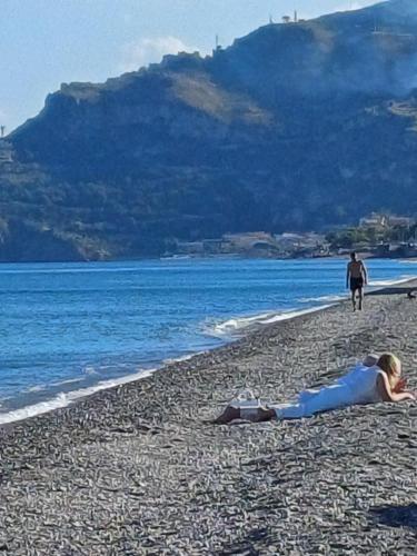 a woman laying on a beach next to the water at Borgo Marino casa vacanze in Santa Teresa di Riva