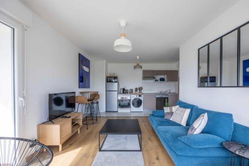 un salon avec un canapé bleu et une cuisine dans l'établissement Superbe appartement neuf avec un grand balcon - Cabourg - Welkeys, à Cabourg