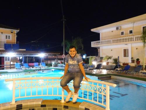 a young boy sitting on a rail next to a swimming pool at Two Brothers Studios Tsilivi Zakynthos in Tsilivi