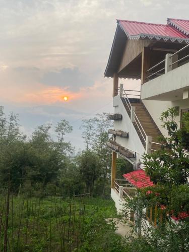 een gebouw met de zonsondergang op de achtergrond bij Bloomfield Farmhouse and Eco-Resort in Darjeeling