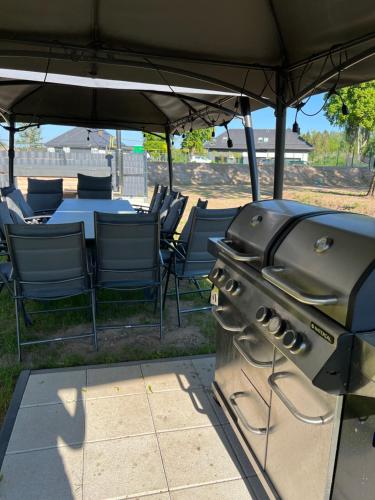 a grill sitting under an umbrella with chairs and a table at Mazurskie Niebo Apartament 1 in Gołdap