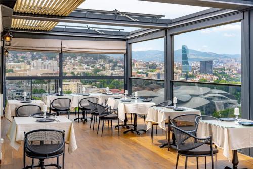 a restaurant with white tables and chairs and large windows at Iris Hotel in Tbilisi City