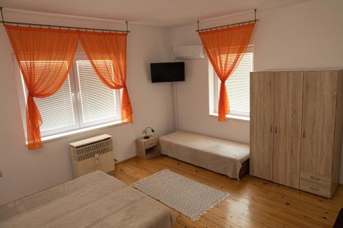 Vínny dom - Rumcajz - Borház في Obid: غرفة نوم بسريرين ونوافذ مع ستائر برتقالية