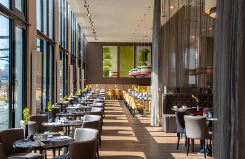 un restaurante con mesas, sillas y ventanas grandes en Leonardo Royal Hotel Munich, en Múnich