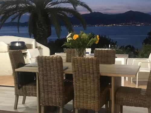 une table à manger avec des chaises en osier et une vue sur l'océan dans l'établissement Villa Sampiero, sur mer, piscine et plage à pieds, à Pietrosella