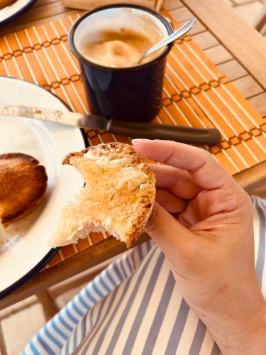 une main tenant un morceau de pain avec une tasse de café dans l'établissement Agriturismo Le Site, à Corigliano dʼOtranto