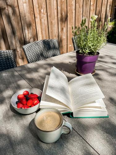 a book and a cup of coffee and a bowl of strawberries at Vila Ambasada in Šventoji