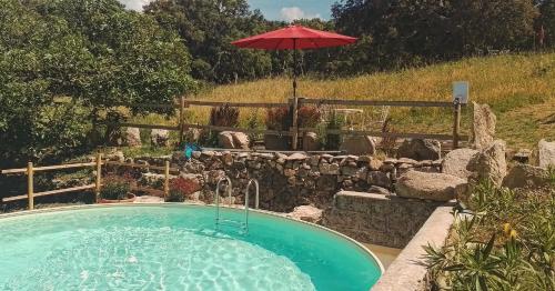 a pool with an umbrella next to a rock wall at Eco Lodge nella natura Con Piscina privata "La Grande Quercia" in Calangianus