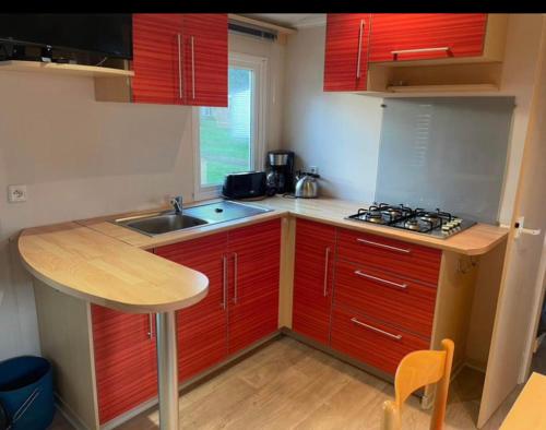 une petite cuisine avec des armoires rouges et un évier dans l'établissement Mobil home 6 personnes sur camping, à La Boissière-de-Montaigu