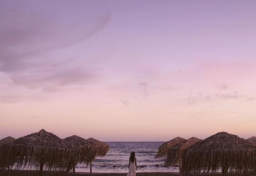 a woman walking on the beach with straw umbrellas at The GrandResort - Limited Edition by Leonardo Hotels in Limassol