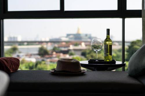 a bottle of wine and a hat on a table with a window at WE HOTEL RIVERFRONT in Bang Su
