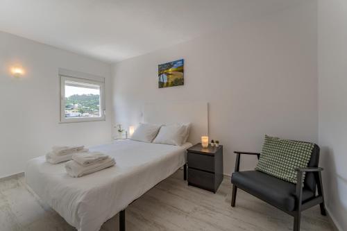 a white bedroom with a bed and a chair at Casa da Quinta in Foz do Sousa