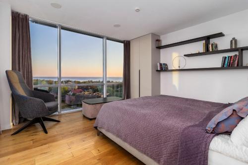 a bedroom with a bed and a chair and large windows at Elija Penthouse in Palanga