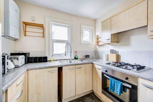 een keuken met houten kasten, een wastafel en een fornuis bij GuestReady - Harrow Delight near Recreation Ground in Londen