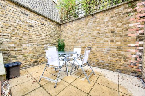 drie stoelen en een tafel voor een stenen muur bij GuestReady - Bright Terrace House in Maida Hill in Londen