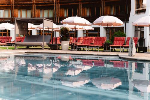 a swimming pool with red chairs and umbrellas at Hotel Die Post in Bad Kleinkirchheim