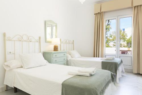 a white bedroom with two beds and a window at Luminoso y amplio piso en Chipiona 5 in Chipiona