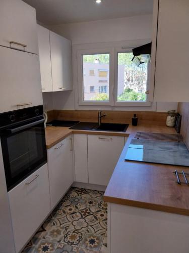 une cuisine avec des armoires blanches, un évier et une fenêtre dans l'établissement Appartement à 300m de la plage, à Fréjus