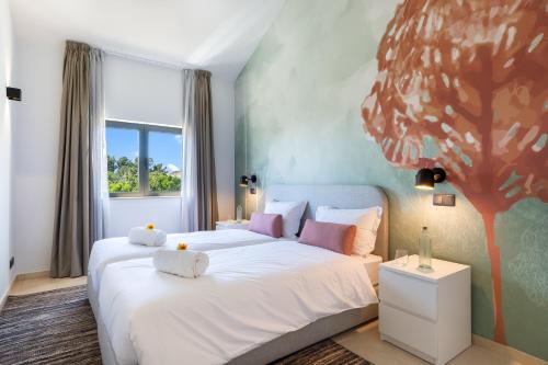 a bedroom with a white bed with a tree painted on the wall at Carvoeiro Gardens in Carvoeiro