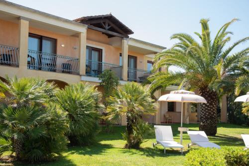 a yard with chairs and an umbrella and palm trees at Hotel Santa Gilla in Capoterra