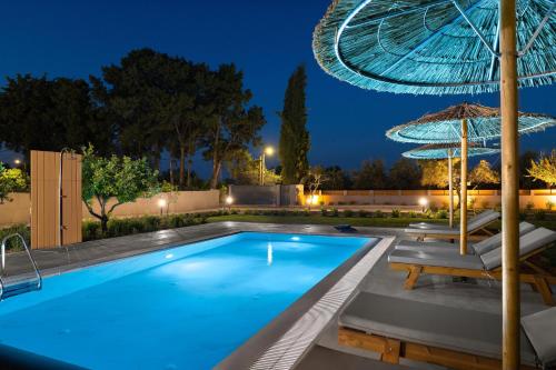 ein Pool in der Nacht mit einem Sonnenschirm und Stühlen in der Unterkunft Villa Ethria Rhodes in Afandou