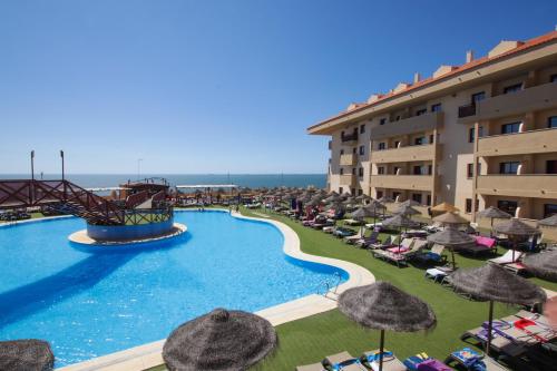 un resort con piscina attrezzata con sedie e ombrelloni di Ohtels Mazagon a Mazagón
