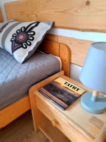 a bed with a table with a lamp and a book at Przy Szlaku Zakopane centrum pokoje & apartamenty in Zakopane