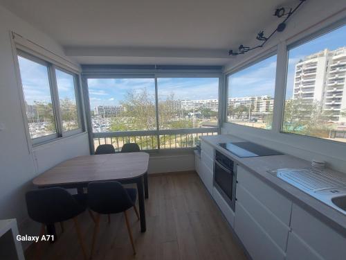 une cuisine avec une table, des chaises et des fenêtres dans l'établissement Studio vue port à 50m plage, à Carnon-Plage