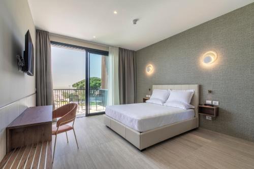a bedroom with a bed and a desk and a balcony at Hotel Gallia & Resort in Lido di Jesolo