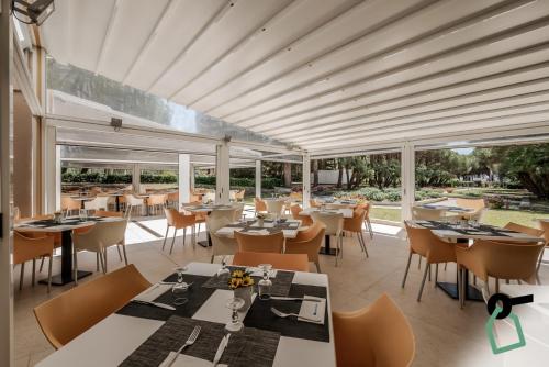 un restaurante con mesas, sillas y ventanas grandes en HOTIDAY Hotel Isola D'Elba en Lacona