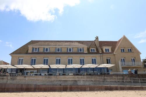 um grande edifício com mesas e guarda-sóis na praia em Le Clos Normand em Saint-Aubin-sur-Mer
