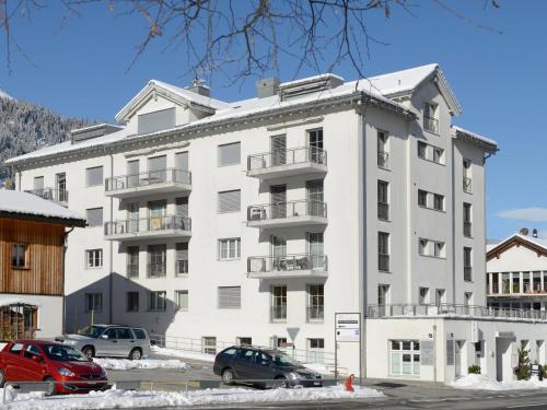 ein weißes Gebäude mit Autos auf einem Parkplatz in der Unterkunft Apartment Moser by Interhome in Churwalden