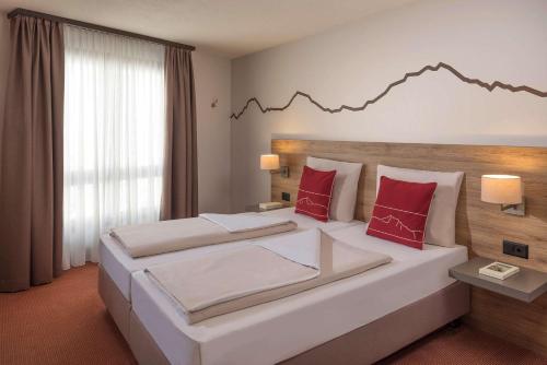 a hotel room with a large bed with red pillows at Dorint Blüemlisalp Beatenberg/Interlaken in Beatenberg