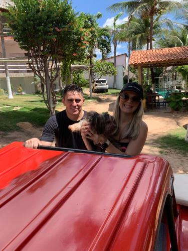 a man and a woman holding a dog in a red car at Ville Sweet Home in Canoa Quebrada