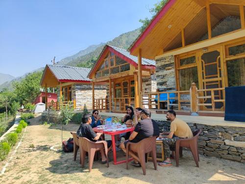 Un groupe de personnes assises à une table devant une maison dans l'établissement Cliff Haven Tirthan, à Banjār