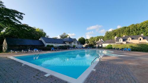 une grande piscine avec des chaises et une maison dans l'établissement Cottage paisible au coeur du golf saint Laurent , linge de maison et ménage inclus, à Ploemel