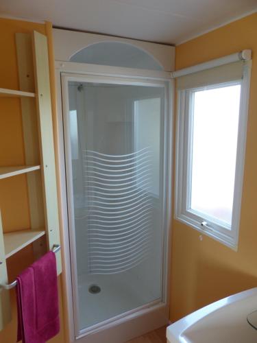 La salle de bains est pourvue d'une douche en verre et d'une fenêtre. dans l'établissement Le Repos du Baigneur - Mobile Home à Soulac sur Mer, à Soulac-sur-Mer