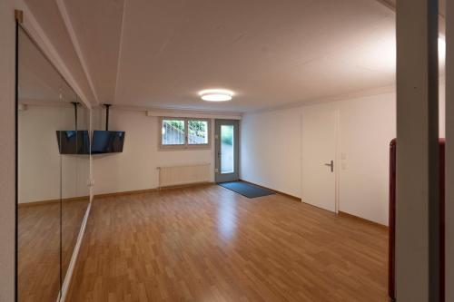 an empty room with a flat screen tv and a wooden floor at Villa with pool, garden & direct at lake in Spiez