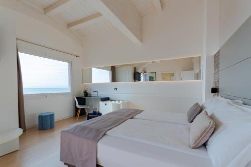 a white bedroom with a large bed and a large window at Hotel Lux in Caorle