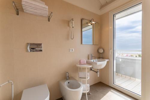 ein Bad mit einem WC, einem Waschbecken und einem Fenster in der Unterkunft Hotel Lux in Caorle