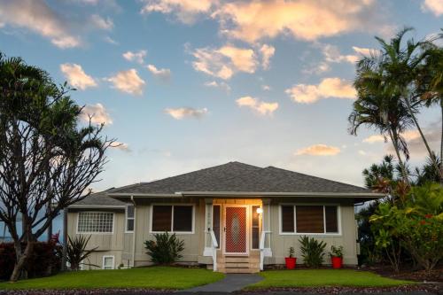 a house with palm trees and a cloudy sky at Kailua-Kona Exceptional Oceanview Home - Heated Oasis Pool & Stunning Ocean View in Kailua-Kona