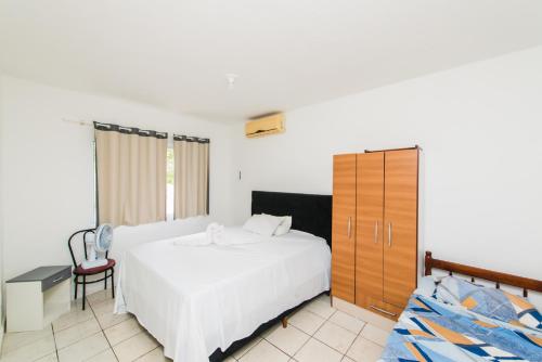 a bedroom with a white bed and a wooden cabinet at Casa Espaçosa com quintal interno in Palhoça