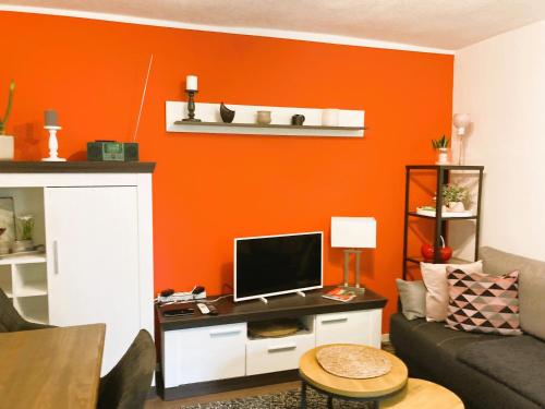 a living room with an orange accent wall at Ferienwohnung Schickolores in Eibenstock