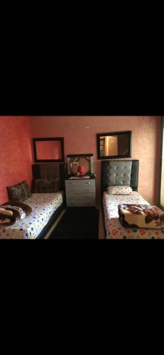 a bedroom with two beds and a dresser and two windows at Location prestigia plage des nations in Sidi Bouqnadel